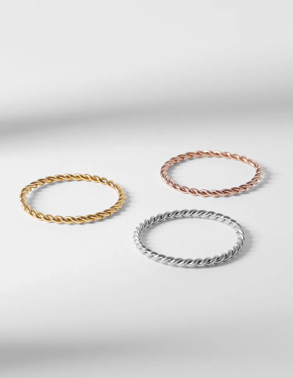 Three braided bracelets in gold, rose gold, and silver on a light gray background