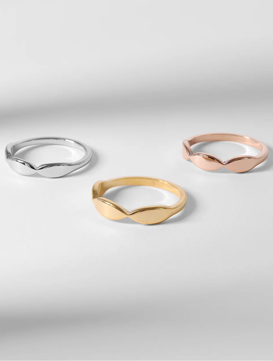Three botanical leaf rings in silver, gold, and rose gold on a light gray background